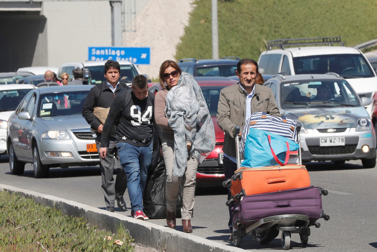 People walk through traffic along a highway as taxi drivers (not pictured) block the way to Santiago's international airport during a protest against Uber and Cabify technologies in Santiago, Chile September 4, 2017. Reuters