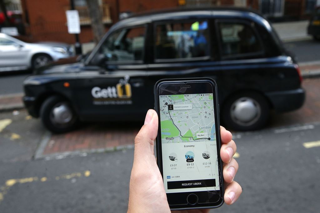 A woman poses holding a smartphone showing the App for ride-sharing cab service Uber in London on September 22, 2017. AFP / Daniel LEAL-OLIVAS
