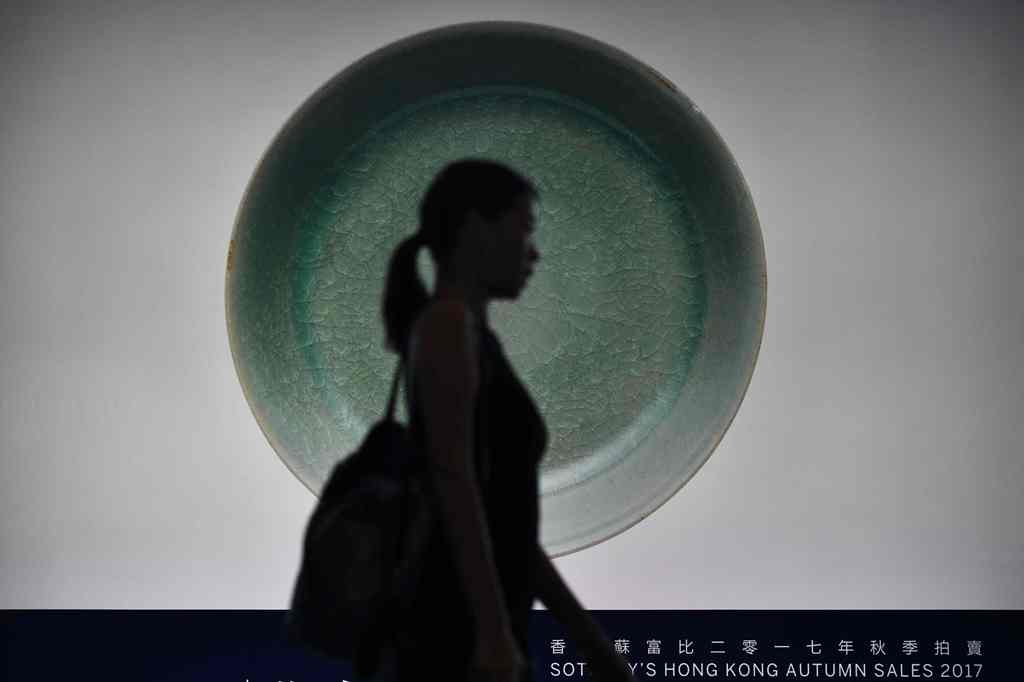 A visitor walks past a backlit photo of a Ru Guanyao brush washer bowl from China's Song Dynasty before its record breaking sale at the Sotheby's Chinese Works of Art Autumn Sales in Hong Kong on October 3, 2017. AFP / Anthony WALLACE