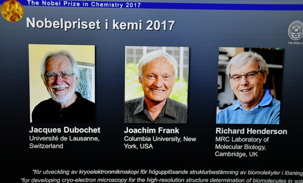 (L-R) Photos of the winners of the Nobel Prize in Chemistry Jacques Dubochet, Joachim Frank and Richard Henderson are seen on a screen as Secretary General of the Royal Swedish Academy of Sciences Goran K. Hansson (not seen) announces the winner of the 20
