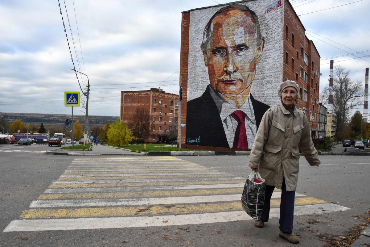 An elderly woman crosses a road in front a mural painting depicting Russian President Vladimir Putin, on the wall of a house, in the town of Kashira, some 115 km southeast of Moscow, on October 16, 2017.  AFP / Vasily Maximov