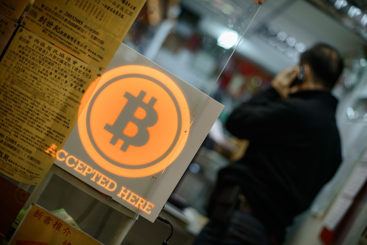 This file picture taken on February 28, 2014 shows a man talking on a mobile phone in a shop displaying a bitcoin sign during the opening ceremony of the first bitcoin retail shop in Hong Kong. AFP/ Philippe Lopez 