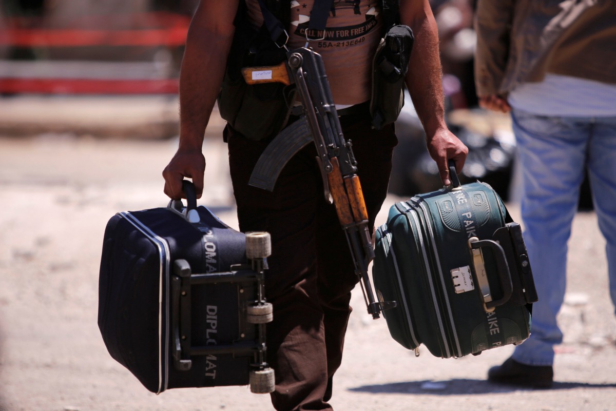 FILE PHOTO: A rebel fighter carries suitcases and his weapon prior to boarding a bus as rebel fighters the besieged Waer district in the central Syrian city of Homs Syria May 21 2017 REUTERS Omar Sanadiki