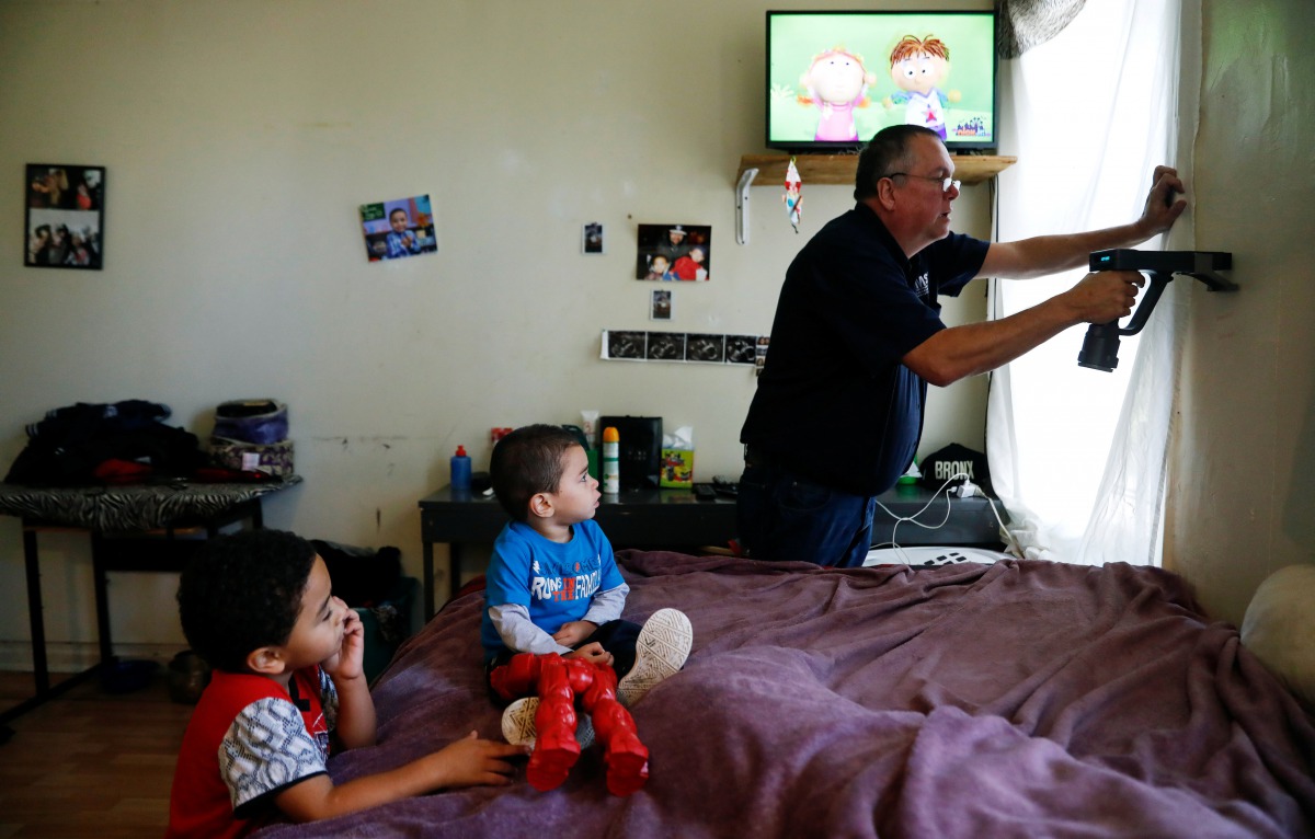 Natalia Rollins children (L) Randy, 4, and Noah,2, watch television as Bob Friedl, a senior project manager with Environmental Management Solutions of New York Inc., checks lead levels with an X-Ray fluorescence detector at their apartment in the Coney Is