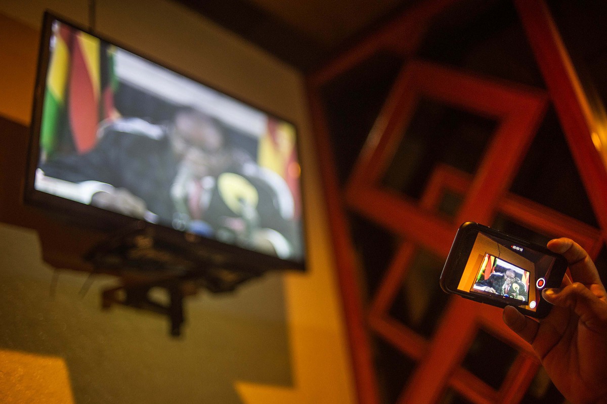 A man uses a mobile phone to record President Robert Mugabe's speech from a television while gathering at The Rainbow Towers in Harare on November 19, 2017. AFP