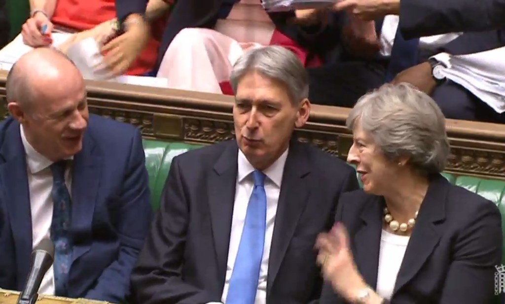 A video grab from footage broadcast by the UK Parliament's Parliamentary Recording Unit (PRU) shows Britain's Chancellor of the Exchequer Philip Hammond (C) with Britain's Prime Minister Theresa May (R) and Britain's Transport Secretary Chris Grayling (L)