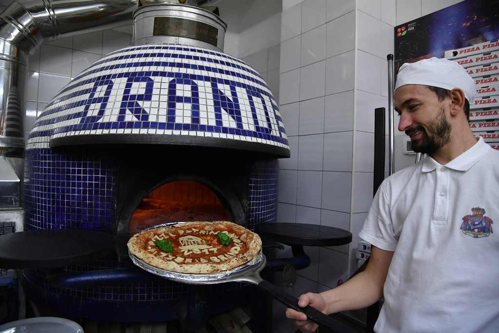 A Neapolitan pizza maker poses next to the oven with a pizza celebrating the Unesco decision to make the art of Neapolitan 