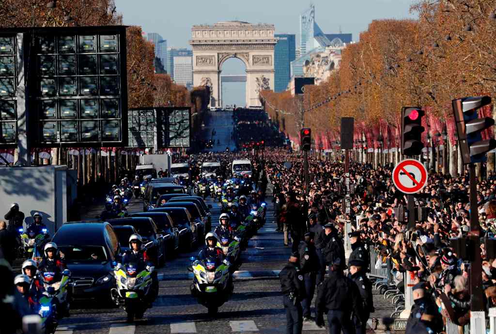 People gather during a 'popular homage' to late French singer Johnny Hallyday as his coffin is driven down the Champs-Elysees avenue on December 9, 2017 in Paris, with the Arc de Triomphe in the background.  AFP / Patrick KOVARIK
