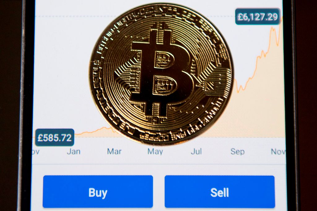 A gold plated souvenir Bitcoin coin is arranged for a photograph on a smart phone displaying current value of a single bitcoin, and options to buy or sell, on an app for the digital asset broker, Coinbase, in London on November 20, 2017.   AFP / Justin TA