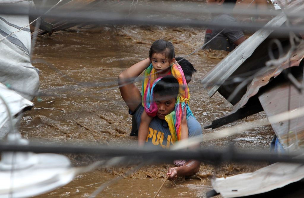 A policeman carries a young girl as he wades through a flooded street in Cagayan City on December 22, 2017, after the Cagayan River swelled caused by heavy rains brought by Tropical Storm Tembin. AFP / Josep DEVEZA