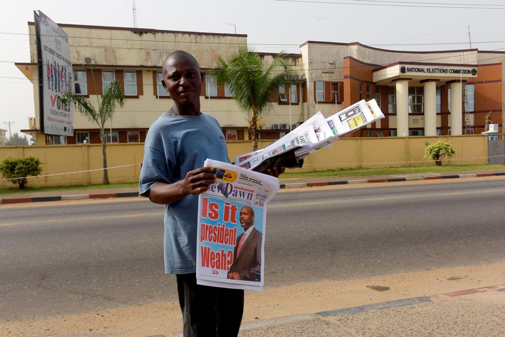 A Liberian newspaper vendor walks in fromt of The National Elections Commission in Monrovia on December 28, 2017.  AFP / SEYLLOU
