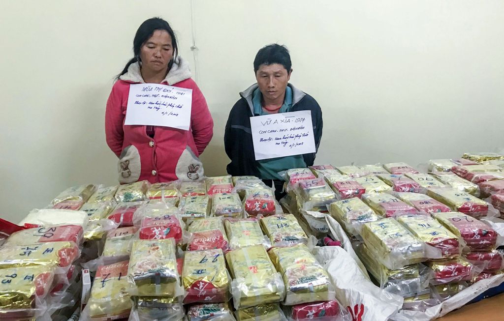 This picture taken on January 2, 2018 shows arrested ethnic H'mong couple Vu Chu Senh (R), 44, and his wife Mua Thi Do, 39, posing behind a table with 489 packs of heroin (170 kgs) they attempted to smuggle into Vietnam from Laos, at a police station in t