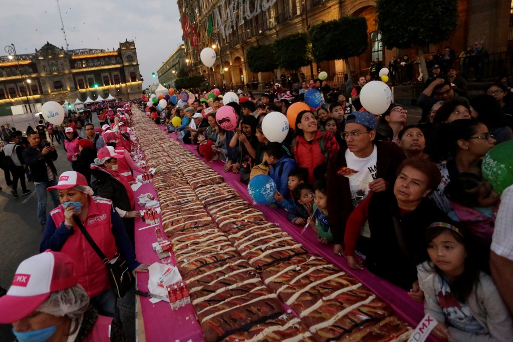 People share balloons as they stand next to a massive cake known as 