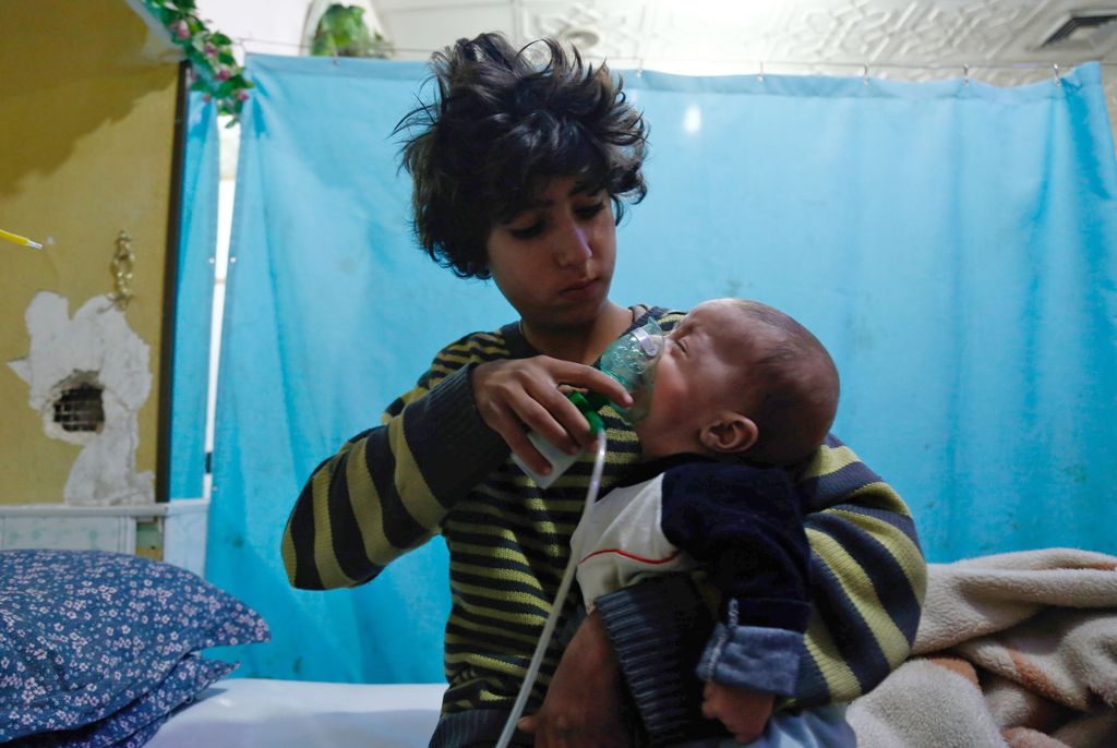 A Syrian boy holds an oxygen mask over the face of an infant at a make-shift hospital following a reported gas attack on the rebel-held besieged town of Douma in the eastern Ghouta region on the outskirts of the capital Damascus on January 22, 2018.  AFP 