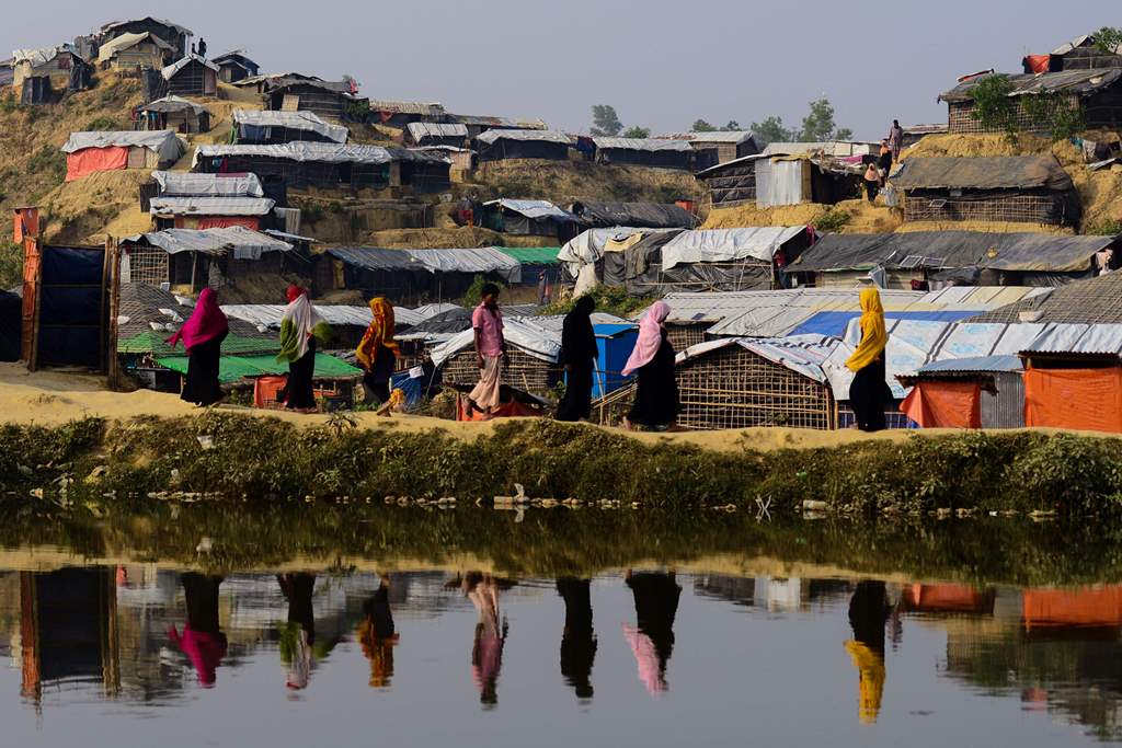(FILES) This file photo taken on November 22, 2017, shows Rohingya refugees are reflected on a pond as they walk back to their homes at Balukhali refugee camp in the Bangladeshi district of Ukhia. AFP / Munir Uz Zaman 