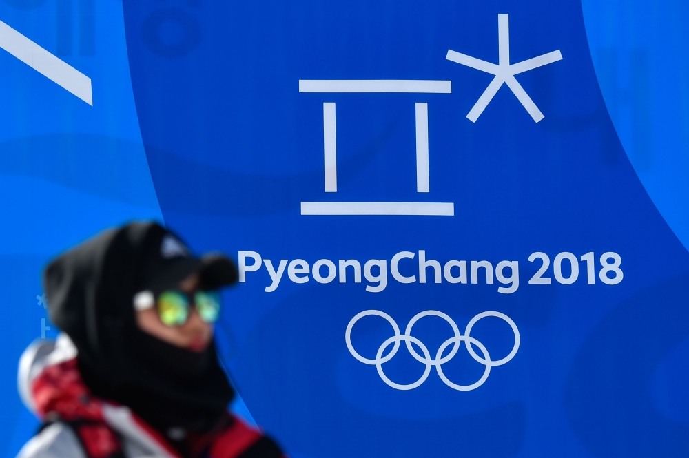 A woman passes past a logo of the the Pyeongchang 2018 Winter olympic Games and the rings, two days prior to the Pyeongchang 2018 Winter olympic Games at the Phoenix Park venue in Pyeongchang on February 6, 2018. / AFP / LOIC VENANCE