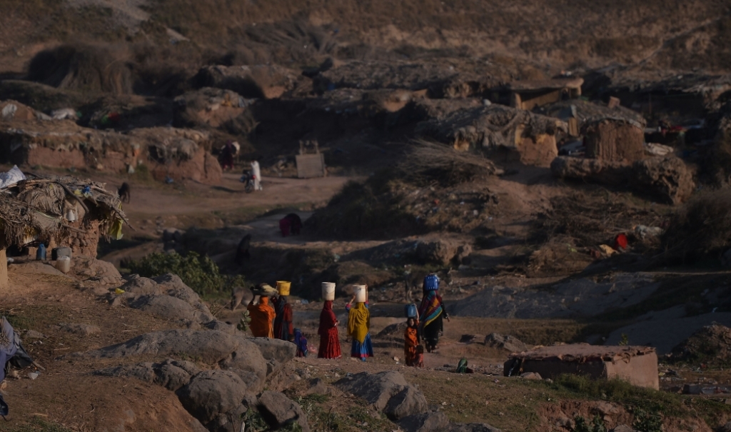 File photo of Afghan refugee women hold water cans on their heads on their way to on their mud houses at a refugee camp in Islamabad, January 19, 2018. / AFP / AAMIR QURESHI /