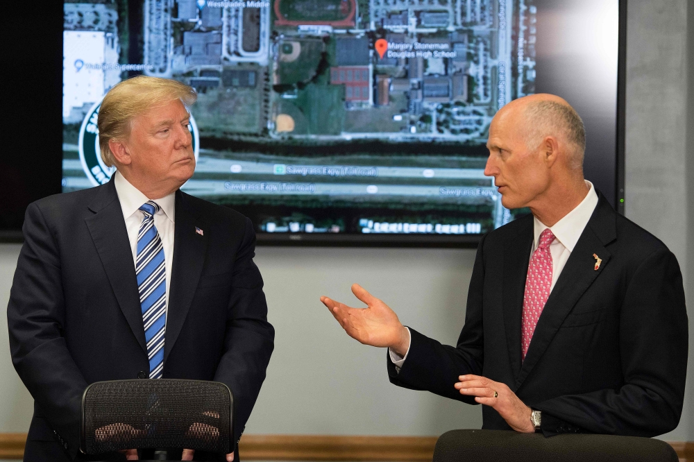 US President Donald Trump (L) speaks with Florida governor Rick Scott (R) while visiting first responders at Broward County Sheriff's Office in Pompano Beach, Florida, on February 16, 2018, three days after a mass shooting that claimed 17 lives at a nearb