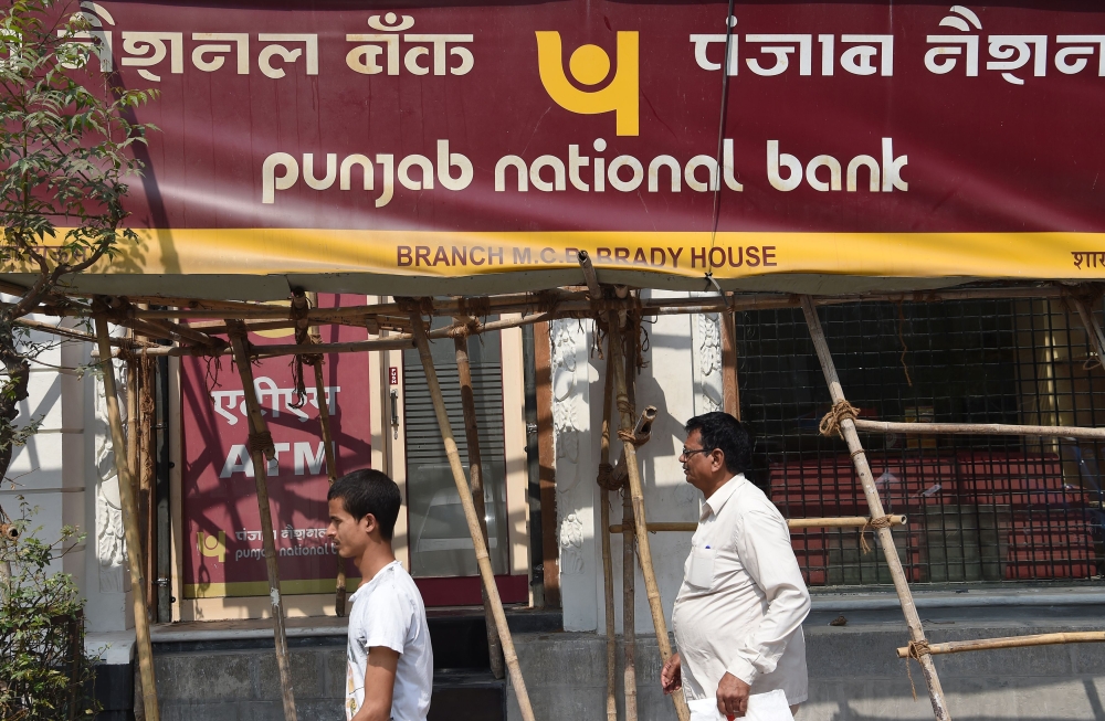 File photo of Indian men walking past signage for the state-owned Punjab National Bank (PNB) in Mumbai on February 14, 2018. / AFP / INDRANIL MUKHERJEE 