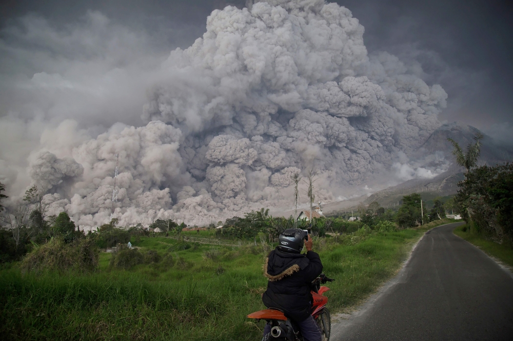 An Indonesian man takes picture of Mount Sinabung volcano as it spews thick volcanic ash into the air in Karo, North Sumatra, on February 19, 2018. AFP / Endro Rusharyanto 