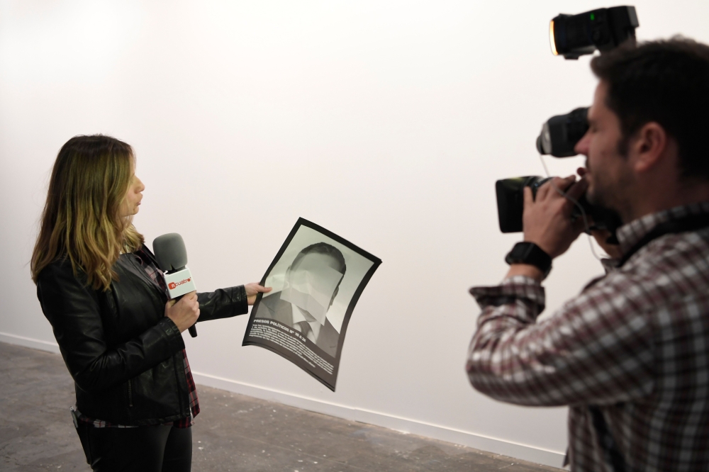 A journalist holds a photograph, part of the art-installation by Spanish artist Santiago Sierra 'Political prisoners of contemporary Spain' as she informs on its removal from ARCO art fair in Madrid on February 21, 2018. AFP / Gabriel Bouys
