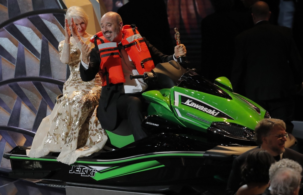 Best Costume Design winner Mark Bridges rides a jet ski onto the stage with actress Helen Mirren on the back after he won it for the shortest Oscar acceptance speech of 2018. REUTERS/Lucas Jackson