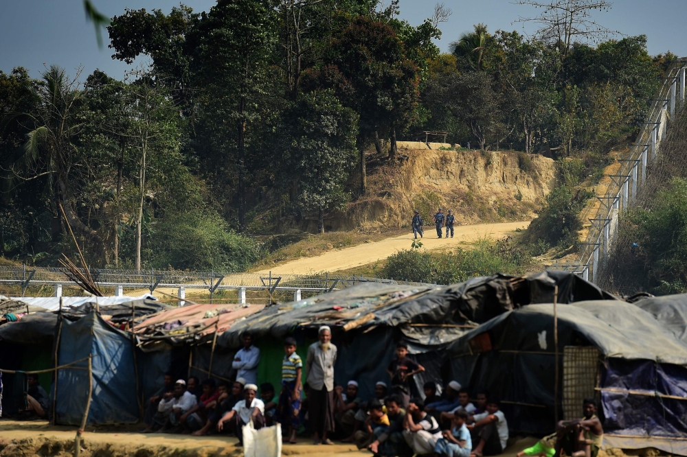 A Myanmar security personnel keeps watch along the Myanmar-Bangladesh border as Rohingya refugee sit outside their makeshifts shelters near Tombru, in the Bangladeshi district of Bandarban on March 1, 2018. AFP / MUNIR UZ ZAMAN