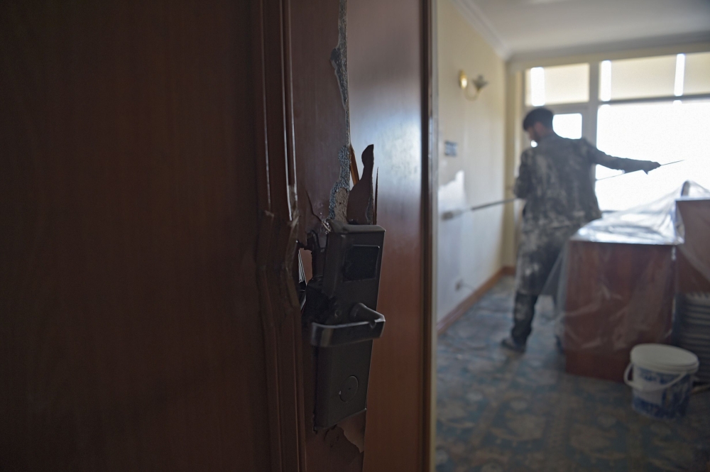 This photograph taken on March 7, 2018 shows an Afghan painter working inside a room with a damaged door at the Intercontinental Hotel in Kabul. AFP / SHAH MARAI 