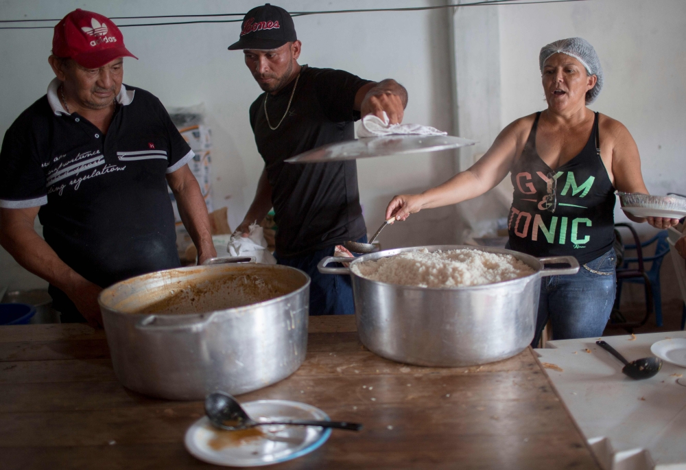 A Venezuelan immigrant (C) helps Brazilian neighborhoods to prepare meals for the Venezuelan refugees living at Simon Bolivar Square, in Boa Vista, Roraima, Brazil, on February 25, 2018.  AFP / Mauro Pimentel
