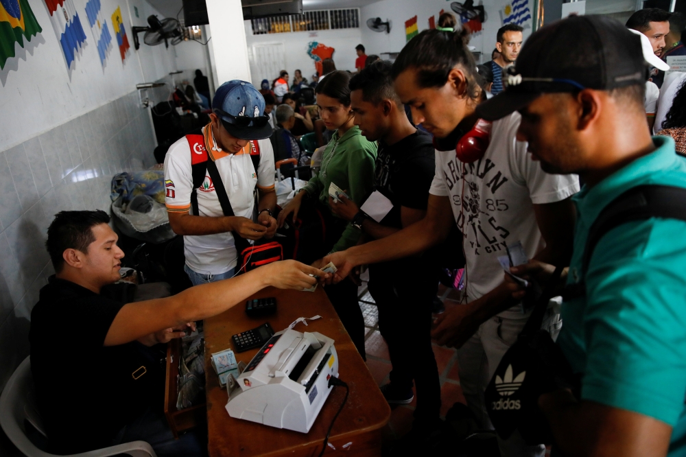 Federico Urquiola (2nd R), 27, a worker in a construction business who is traveling by bus from Caracas to Peru, exchanges money in Cucuta, Colombia, November 8, 2017. Federico said he struggled to get contracts for his construction business and was often