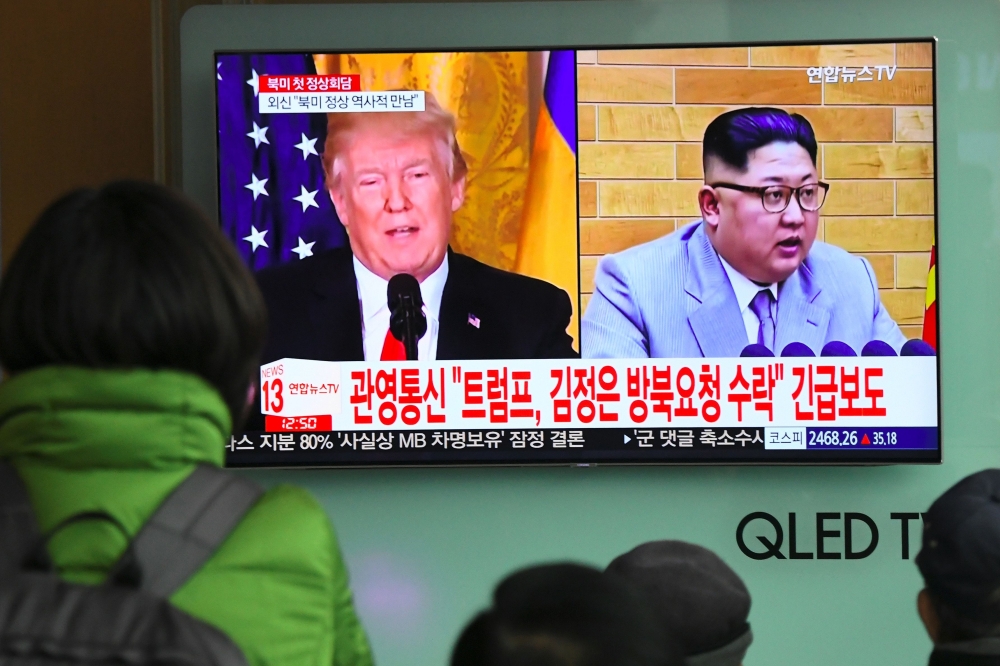 People watch a television news report showing pictures of US President Donald Trump (L) and North Korean leader Kim Jong Un at a railway station in Seoul on March 9, 2018. / AFP / Jung Yeon-je 