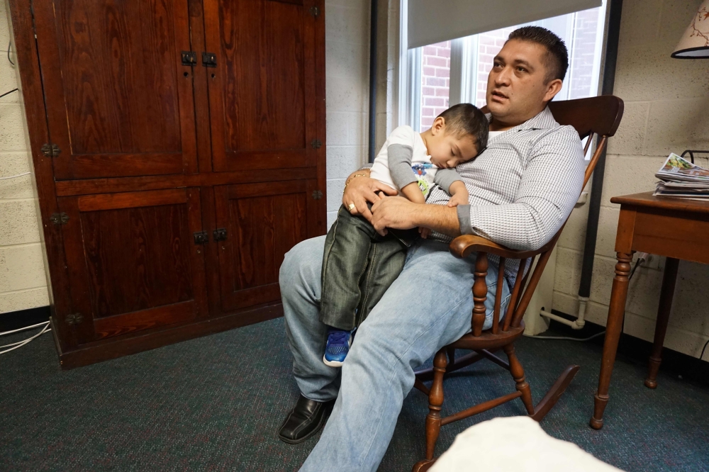Business owner Oscar Canales holds his son, George, as he speaks during an interview at the Congregational United Church of Christ where he is living in sanctuary on February 12, 2018, in Greensboro, North Carolina. 
AFP / Issam Ahmed 