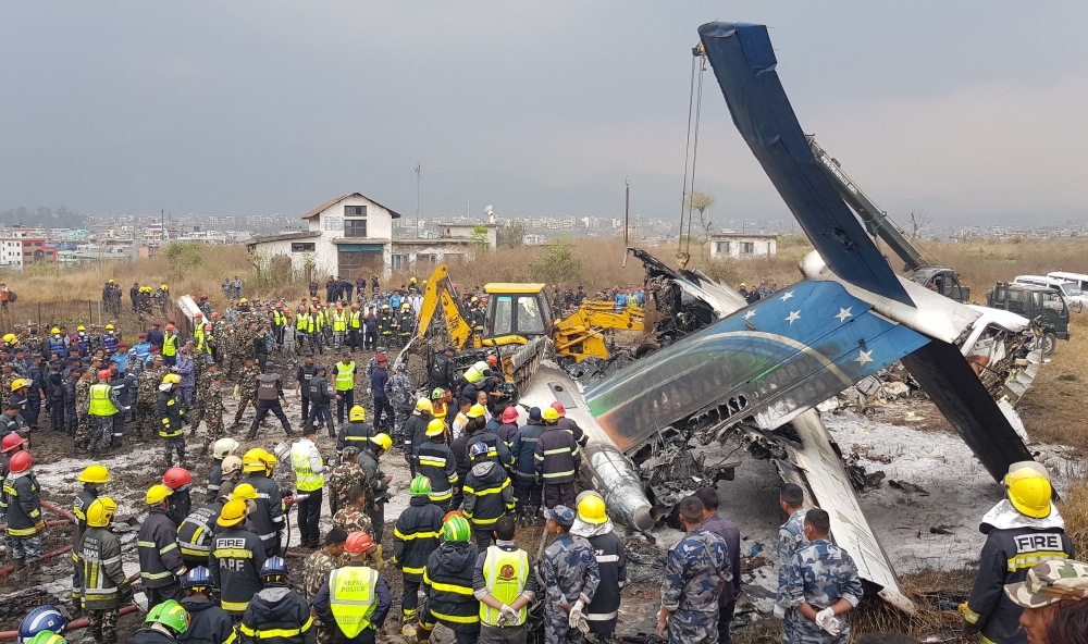 Nepali rescue workers gather around the debris of an airplane that crashed near the international airport in Kathmandu on March 12, 2018. AFP / Prakash Mathema 