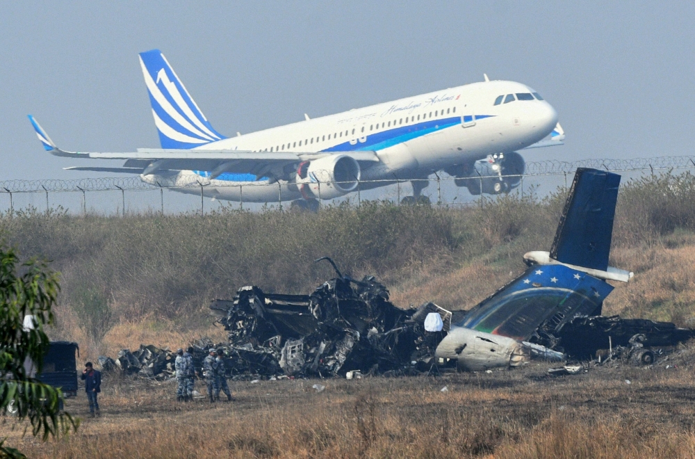 An airplane takes off at the international airport in Kathmandu on March 13, 2018, near the wreckage of a US-Bangla Airlines plane that crashed on March 12. AFP / PRAKASH MATHEMA
