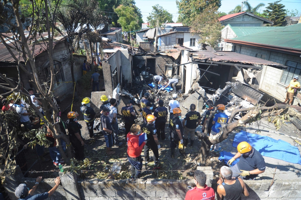 Rescuers and investigators stand at the site where a twin-engine plane crashed into a house just after taking off in Plaridel town, Bulacan province, north of Manila on March 17, 2018.  AFP / STR
