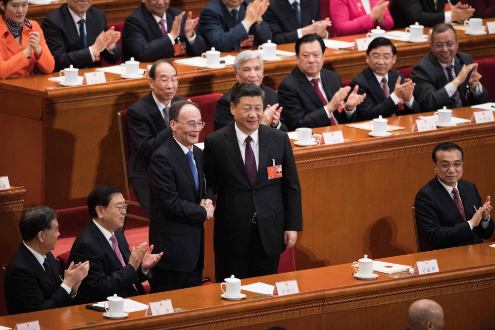 Wang Qishan (C, left), former secretary of the Central Commission for Discipline Inspection, shakes hands with China's President Xi Jinping (C) after Wang was elected as China's Vice President during the fifth plenary session of the first session of the 1