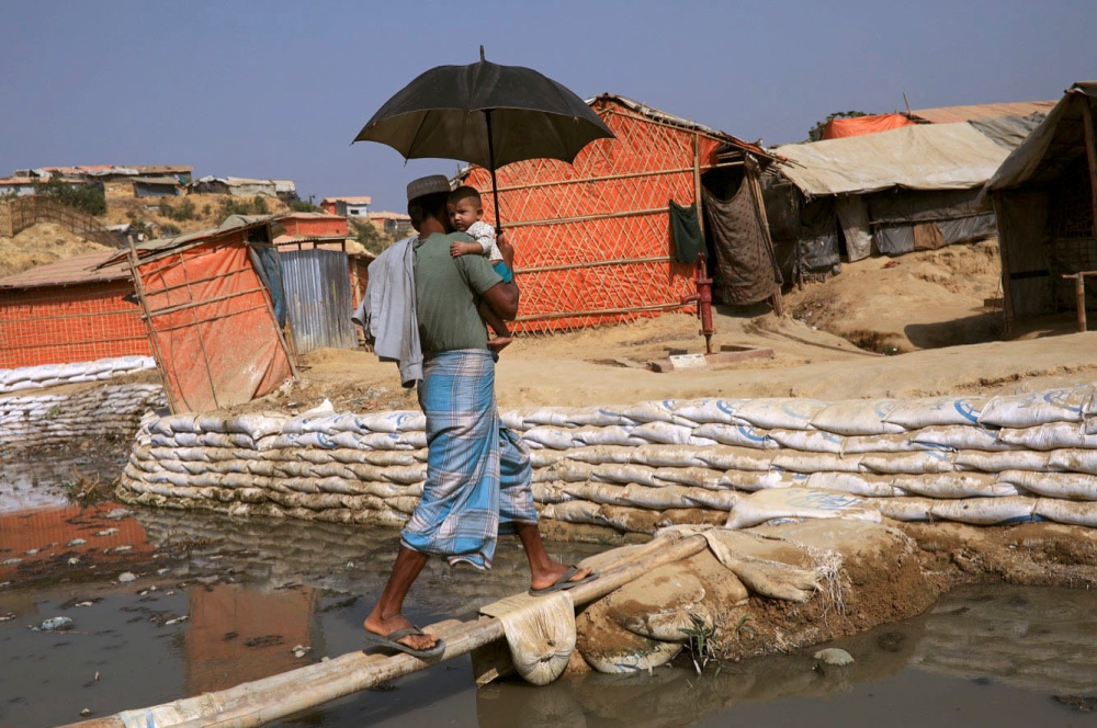 A Rohingya refugee man with child walks on a bamboo bridge to cross a water stream in Balukhali refugee camp, in Cox's Bazar, Bangladesh, March 21, 2018. Reuters/Mohammad Ponir Hossain

