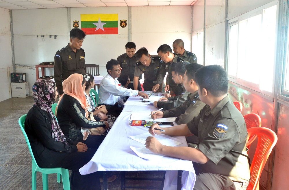 This handout photograph released by Myanmar News Agency on April 15, 2018 and taken April 14, 2018, Myanmar immigration official hands over identification document to an unidentified Rohingya woman belonging to the five member Rohingya family at Taungpyol