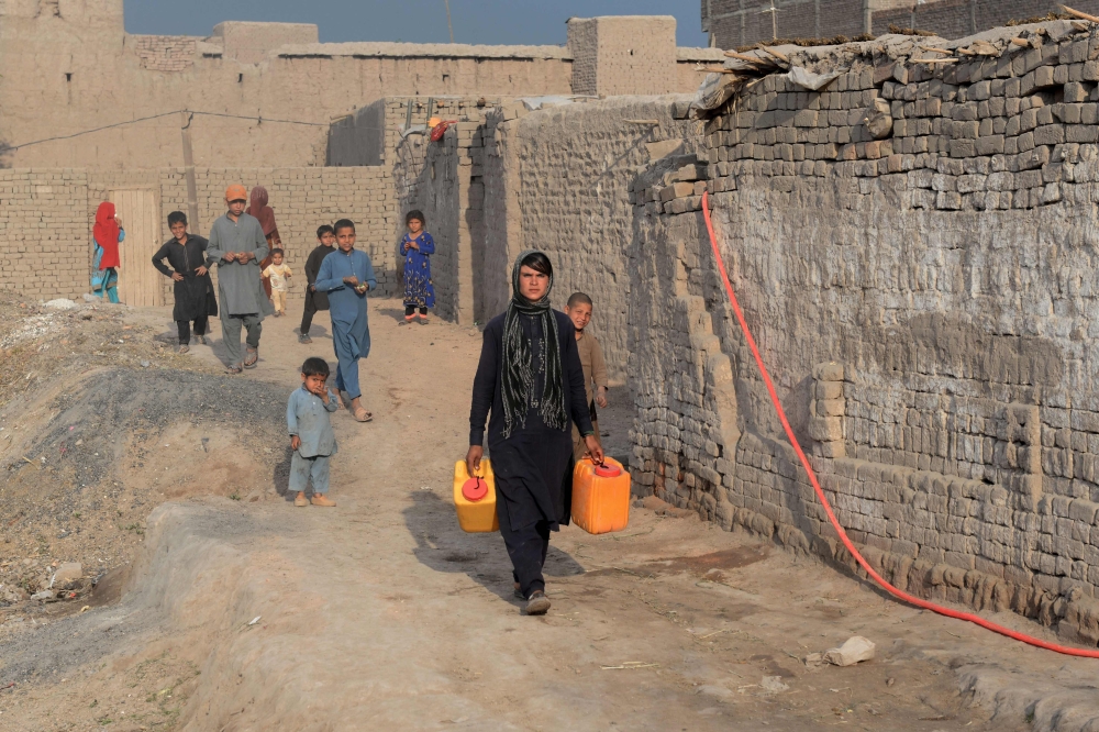 File photo of shows Afghan female labourer Sitara Wafadar, 18, who dresses as a male in order to support her family, collecting water near her home in Sultanpur village in Surkh Rod district, in Afghanistan's eastern Nangarhar province, March 20, 2018. / 