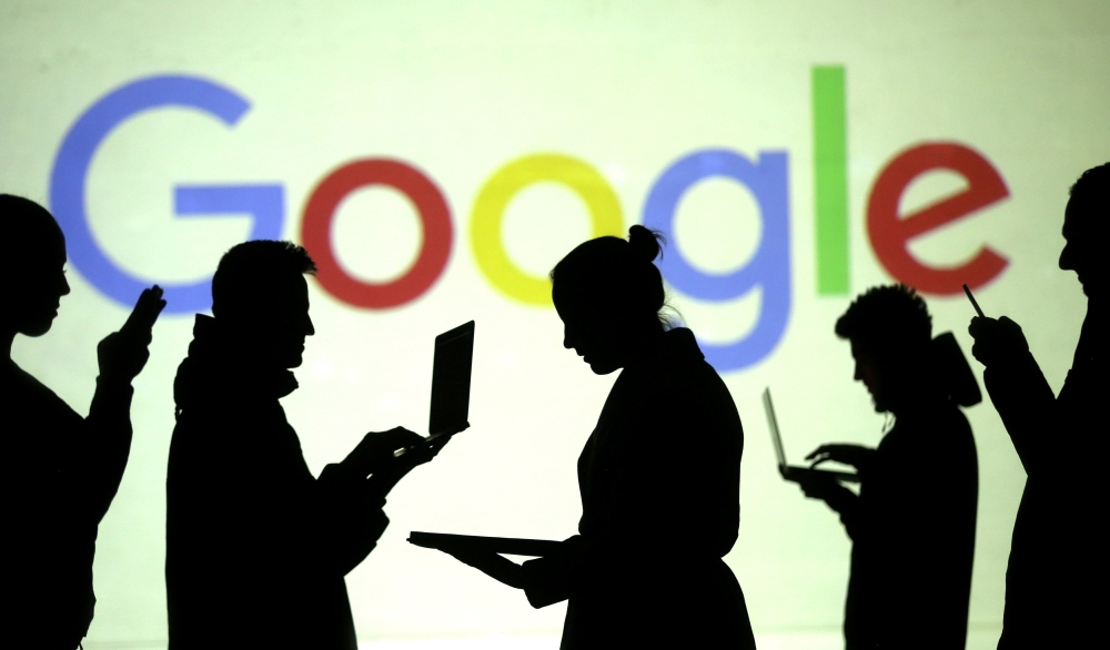Silhouettes of laptop and mobile device users are seen next to a screen projection of Google logo in this picture illustration, March 28, 2018. (Reuters / Dado Ruvic) 