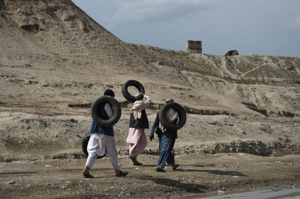 Afghan men carry tires as they walk near the old fortress of Bala Hissar in Kabul on May 6, 2018. / AFP / WAKIL KOHSAR
