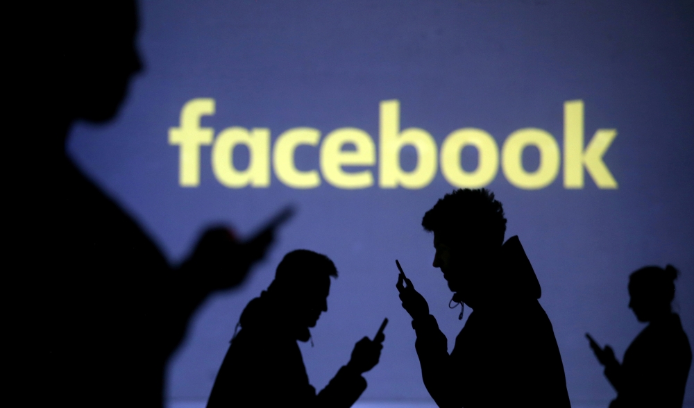 Silhouettes of mobile users are seen next to a screen projection of Facebook logo in this picture illustration taken March 28, 2018. REUTERS/Dado Ruvic/Illustration/File Photo
