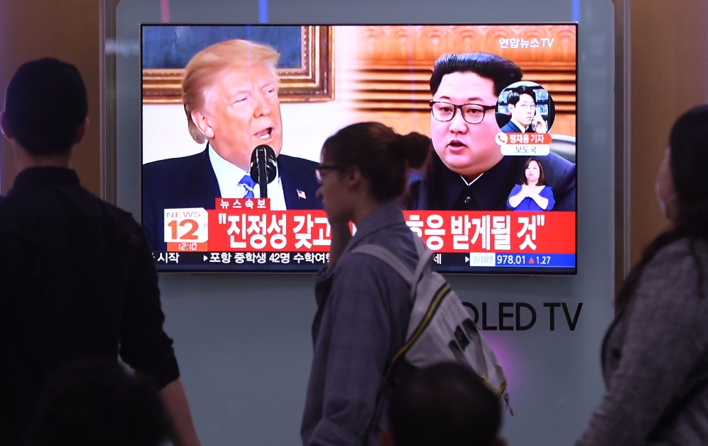 People walk past a television news screen showing North Korean leader Kim Jong Un (R) and US President Donald Trump (L) at a railway station in Seoul on May 16, 2018. AFP / Jung Yeon-je