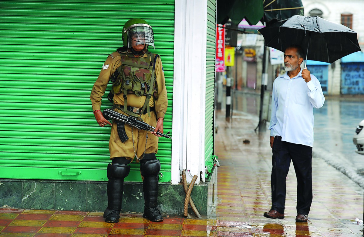 A Kashmiri muslim looks at an Indian paramilitary trooper standing guard amidst a heavy rainfall during a curfew in Srinagar, on July 27, 2016. AFP/ Tauseef Mustafa