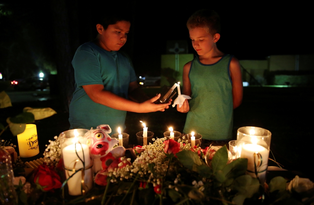 Christian Cardenas 10, helps Jaydon Johnson 8, light a candle during a vigil for the victims of a shooting at Santa Fe High School that left several dead and injured in Santa Fe, Texas, U.S., May 18, 2018. REUTERS/Pu Ying Huang