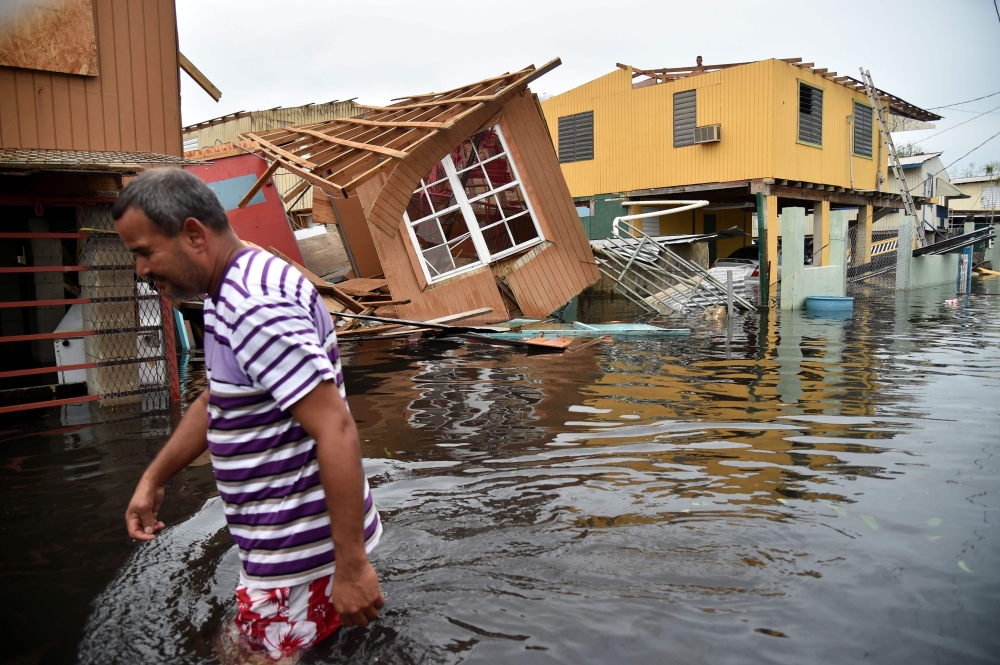 (FILE PHOTO) In this file photo taken on September 21, 2017 a man walks past destroyed homes in Catano, Puerto Rico, on September 21, 2017.  AFP / HECTOR RETAMAL
