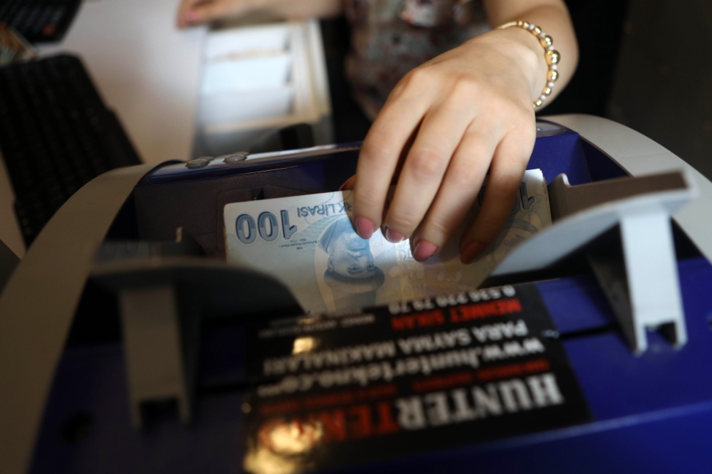 An employee of a foreign exchange office counts and checks Turkish lira banknotes with a machine in the centre of Ankara on May 25, 2018. / AFP / ADEM ALTAN