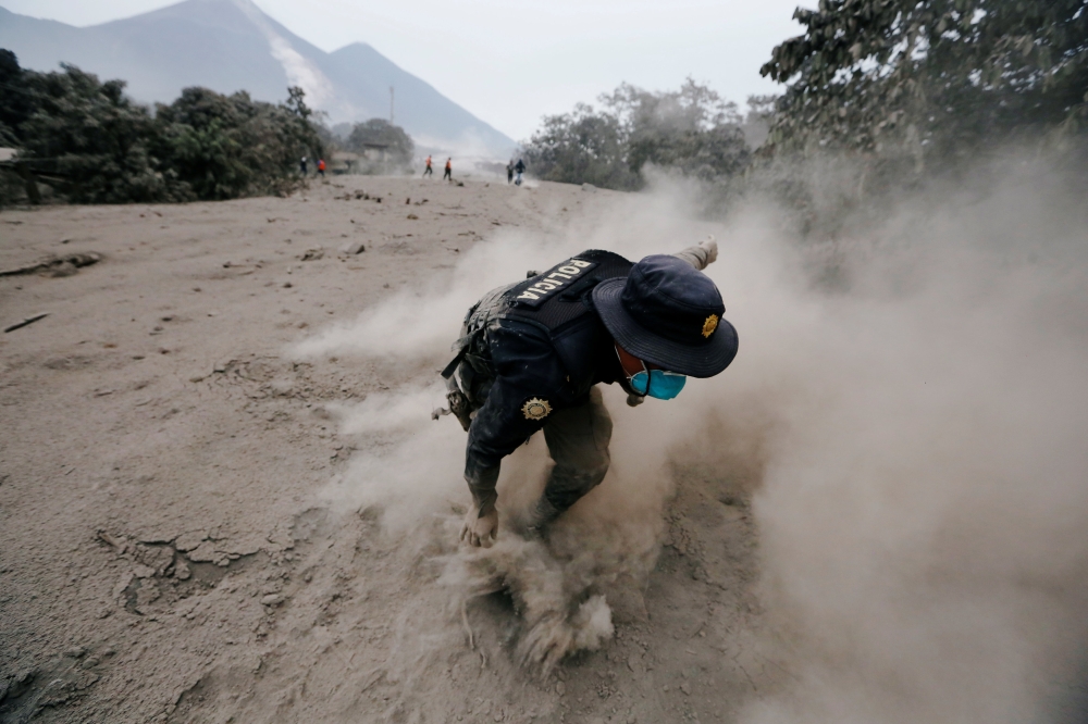 A police officer stumbles while running away after a the Fuego volcano spew new pyroclastic flow in the community of San Miguel Los Lotes in Escuintla, Guatemala, June 4, 2018. REUTERS/Luis Echeverria