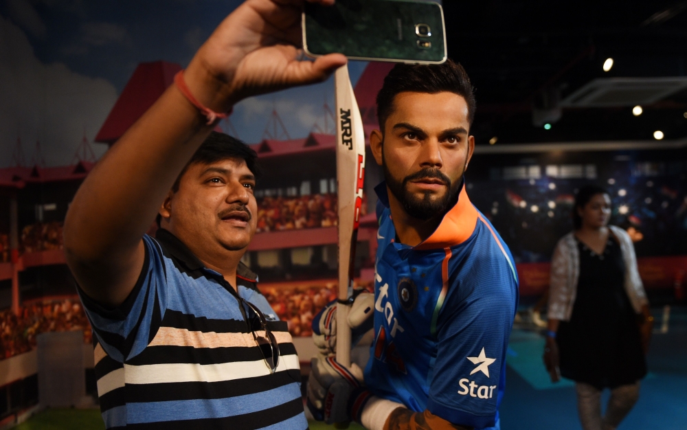 An Indian visitor takes a selfie with the newly unveiled wax statue of Indian cricketer Virat Kohli at the Madame Tussauds Delhi in New Delhi on June 6, 2018. / AFP / MONEY SHARMA