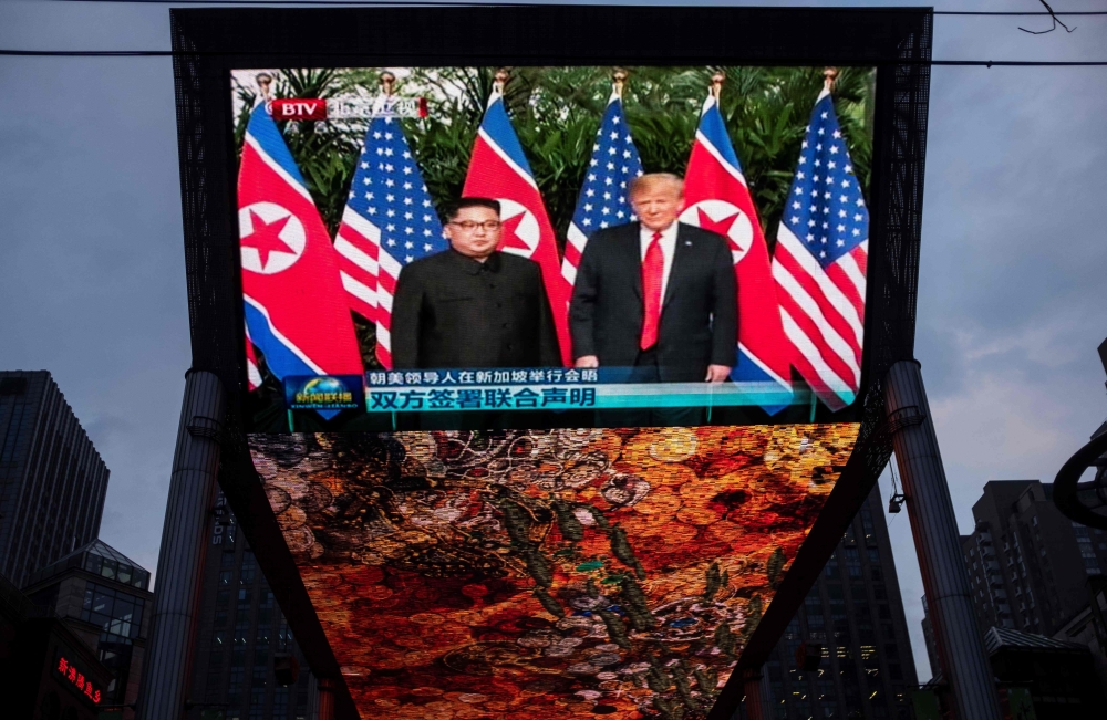 A giant TV screen shows US President Donald Trump (R) and North Korea's leader Kim Jong Un shake hands following a signing ceremony during their historic US-North Korea summit, in Beijing on June 12, 2018. AFP / Johannes EISELE